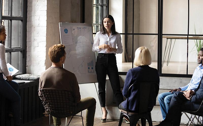 Woman presenting with people sat around looking at whiteboard